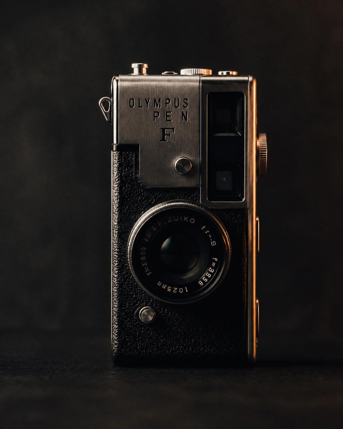 Half-frame film camera with brushed titanium top plate lit by a warm key light